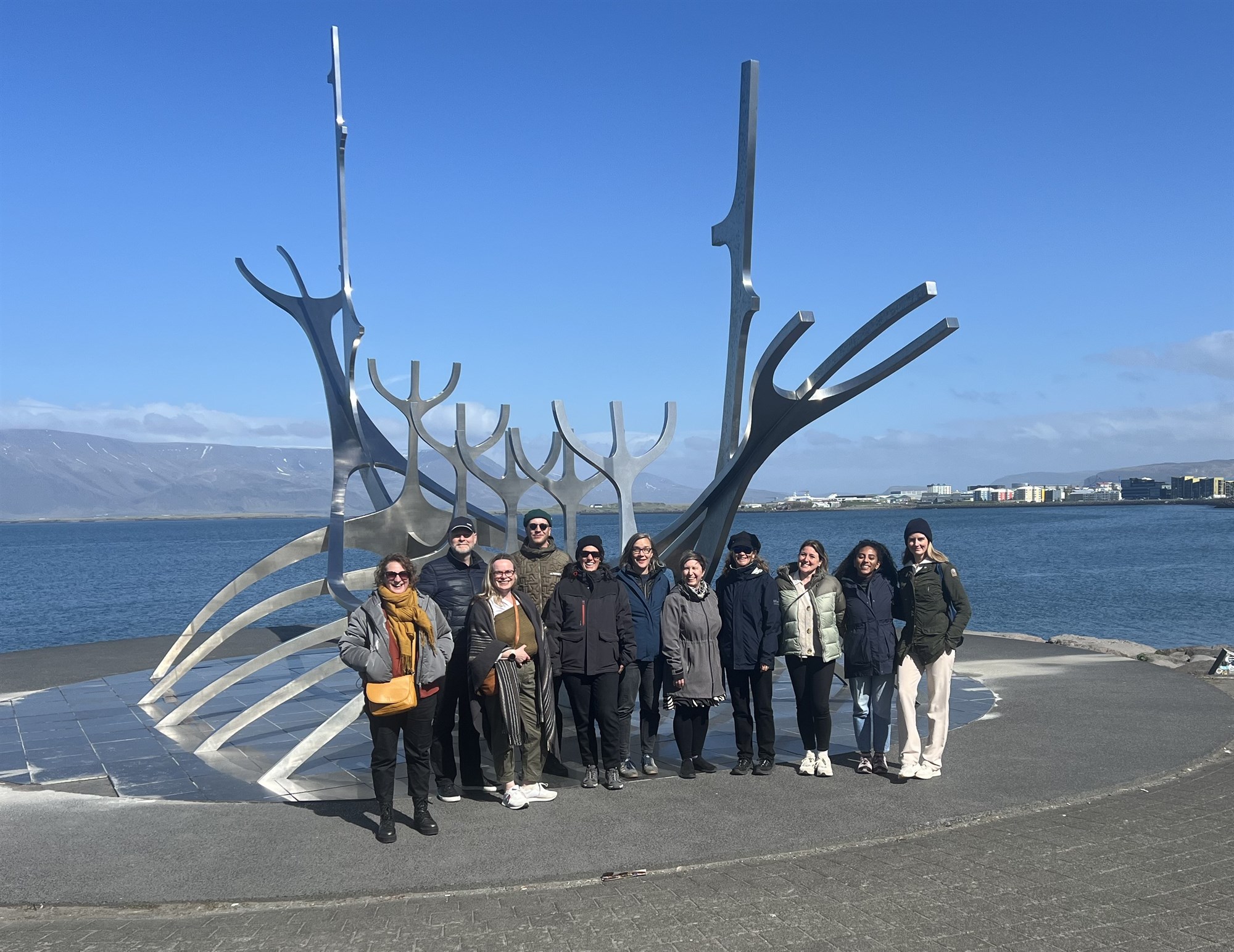 Staff and students standing in front of a viking ship monument by ocean front in Reykjavik